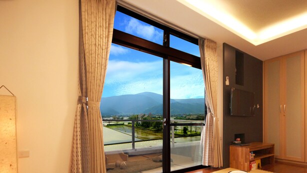 A hotel room with a large sliding glass door leading to a balcony, a flat-screen TV mounted on the wall, and a wooden wardrobe. - Easylife B&B  (Dongshan)