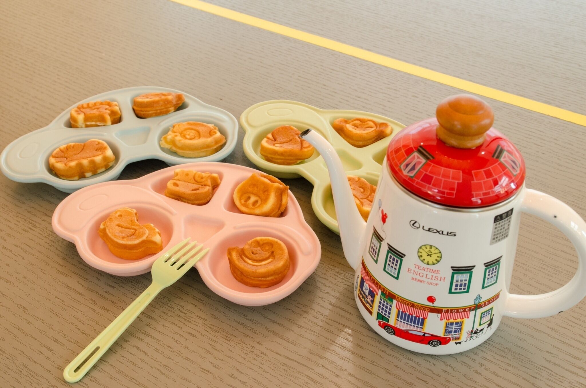 Eine weiße Tasse mit rotem Deckel und farbigem Muster, eine pinke Silikonform mit herzförmigen Ausbuchtungen und eine grüne Silikonform mit kreisförmigen Fächern.