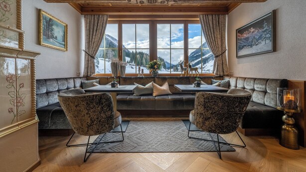 A cozy seating area with a sofa and two chairs, a large window with a view of mountains, and a decorative vase with flowers. - Hotel Montanara (Ischgl)
