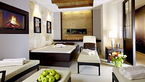 A modern hotel room with a large bed, a sitting area with a view of a fire, a small table with apples, and a vase of flowers. - Hotel Montanara (Ischgl)