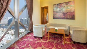 Habitación de hotel con un ventanal grande, dos sillones, un sofá, una mesa de centro de madera y una alfombra estampada.