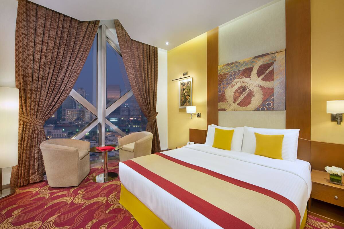 A hotel room with a large bed, a desk, a chair, and a view of the cityscape.