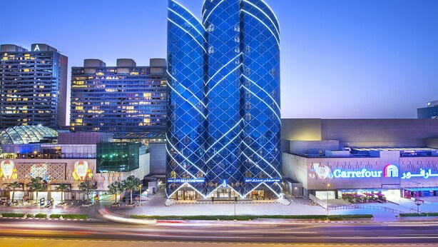 Un hotel moderno con una fachada curva distintiva y un supermercado Carrefour contiguo.