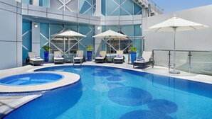 Zona de piscina moderna de hotel con jacuzzi, sillas de descanso y sombrillas.