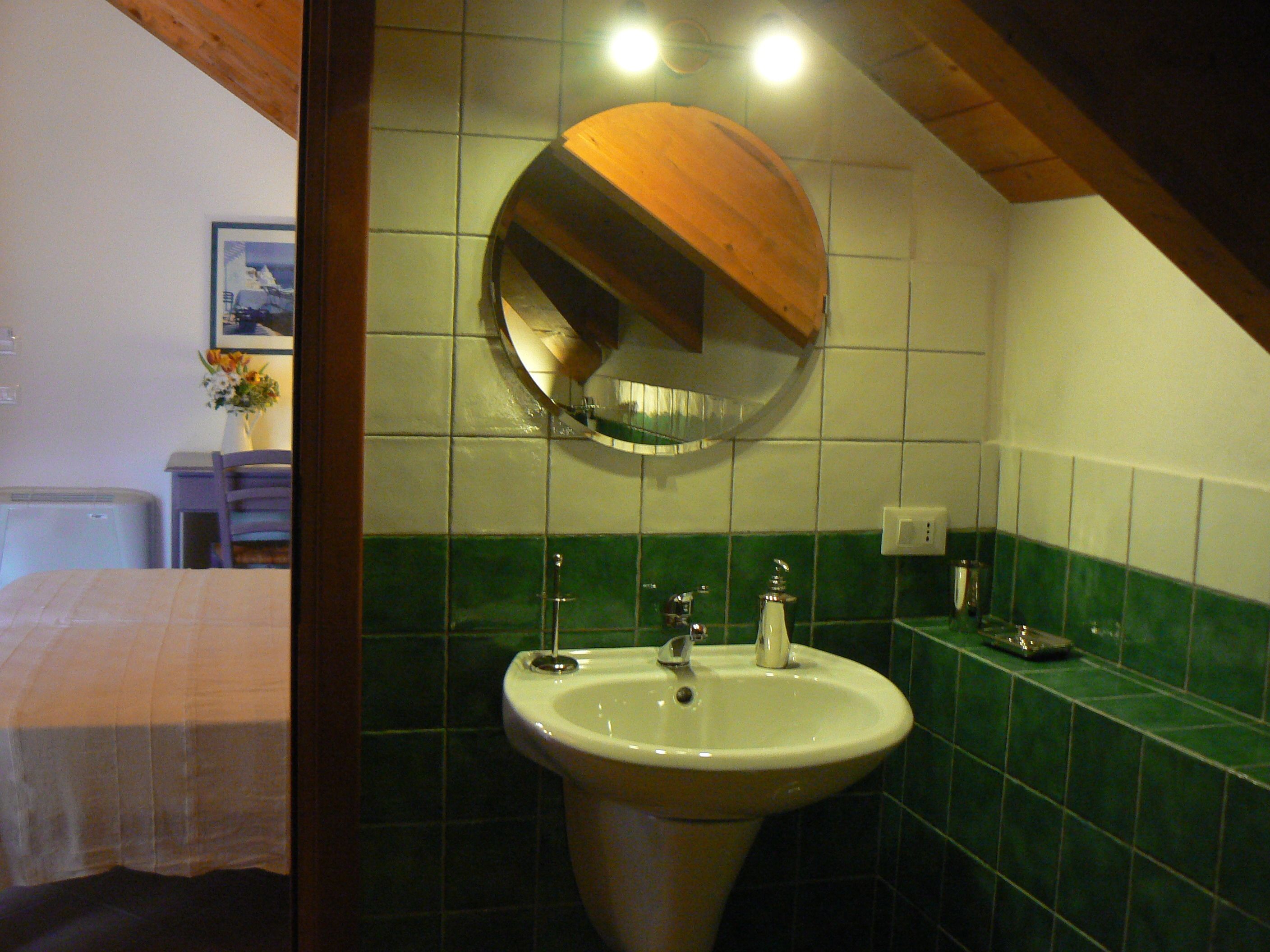 Un baño con lavamanos, espejo y azulejos verdes.