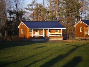 Two wooden cabins with blue roofs, surrounded by a grassy field and trees. - Rip Van Winkle Motel (Plattsburgh)