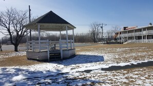 A gazebo with a sloped roof and a fenced perimeter, located in a grassy area with patches of snow. - Rip Van Winkle Motel (Plattsburgh)
