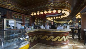 Zona de bar con una barra curva, estanterías con botellas y una vitrina.