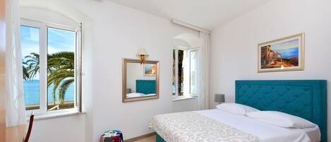 Une chambre à coucher avec un lit, une fenêtre donnant sur des palmiers, un miroir et un tableau accroché au mur.