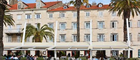A hotel with outdoor seating, palm trees, and a red-tiled roof.