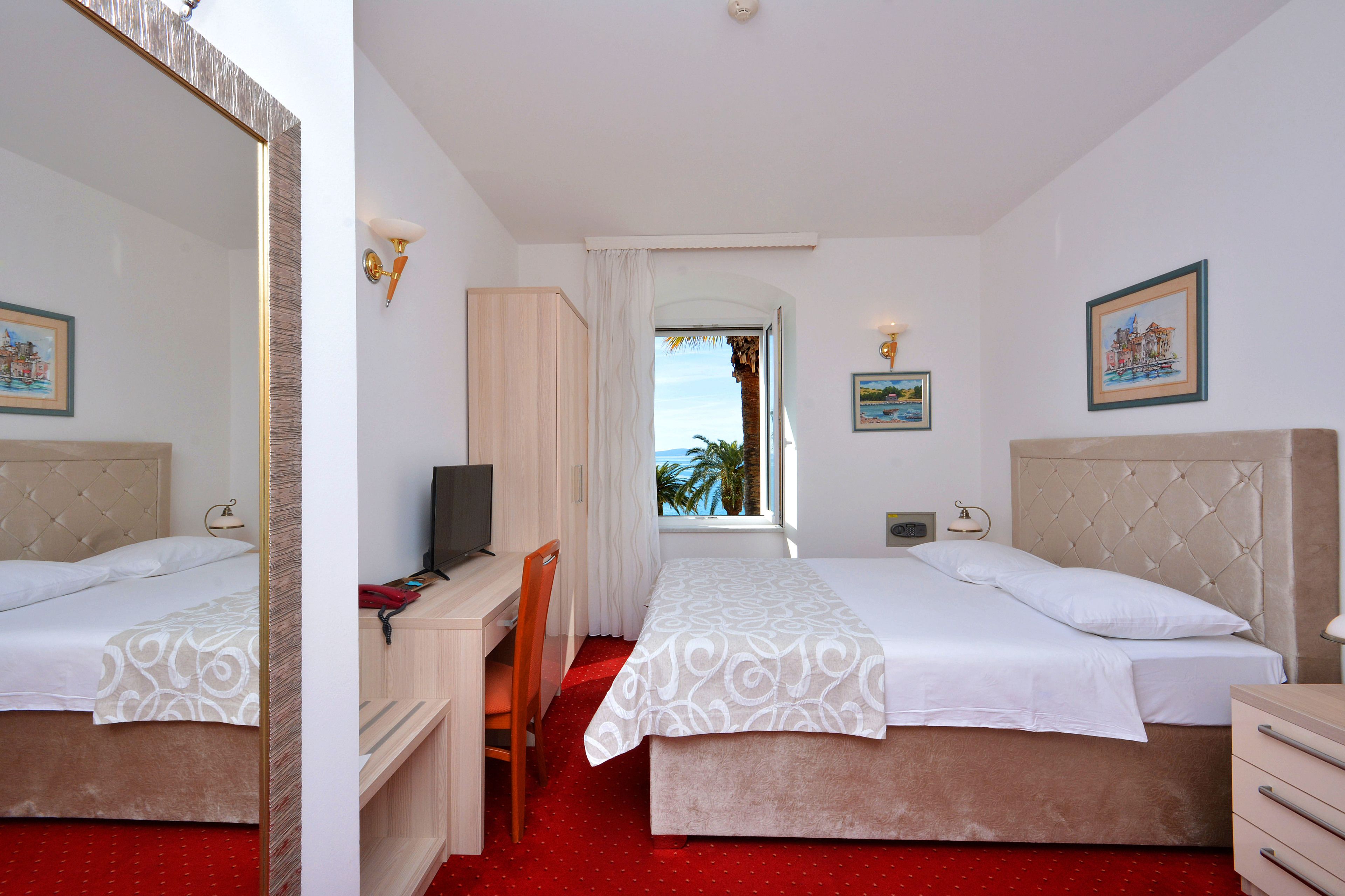 Ein Hotelzimmer mit zwei Betten, einem Schreibtisch, einem Sessel, einem Fernseher und einem Fenster mit Meerblick.