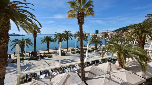 Un paseo marítimo con palmeras, mesas al aire libre y vistas al mar.