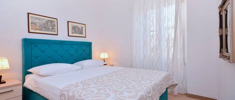 A neatly made bed with a teal headboard, white bedding, and two framed pictures on the wall.