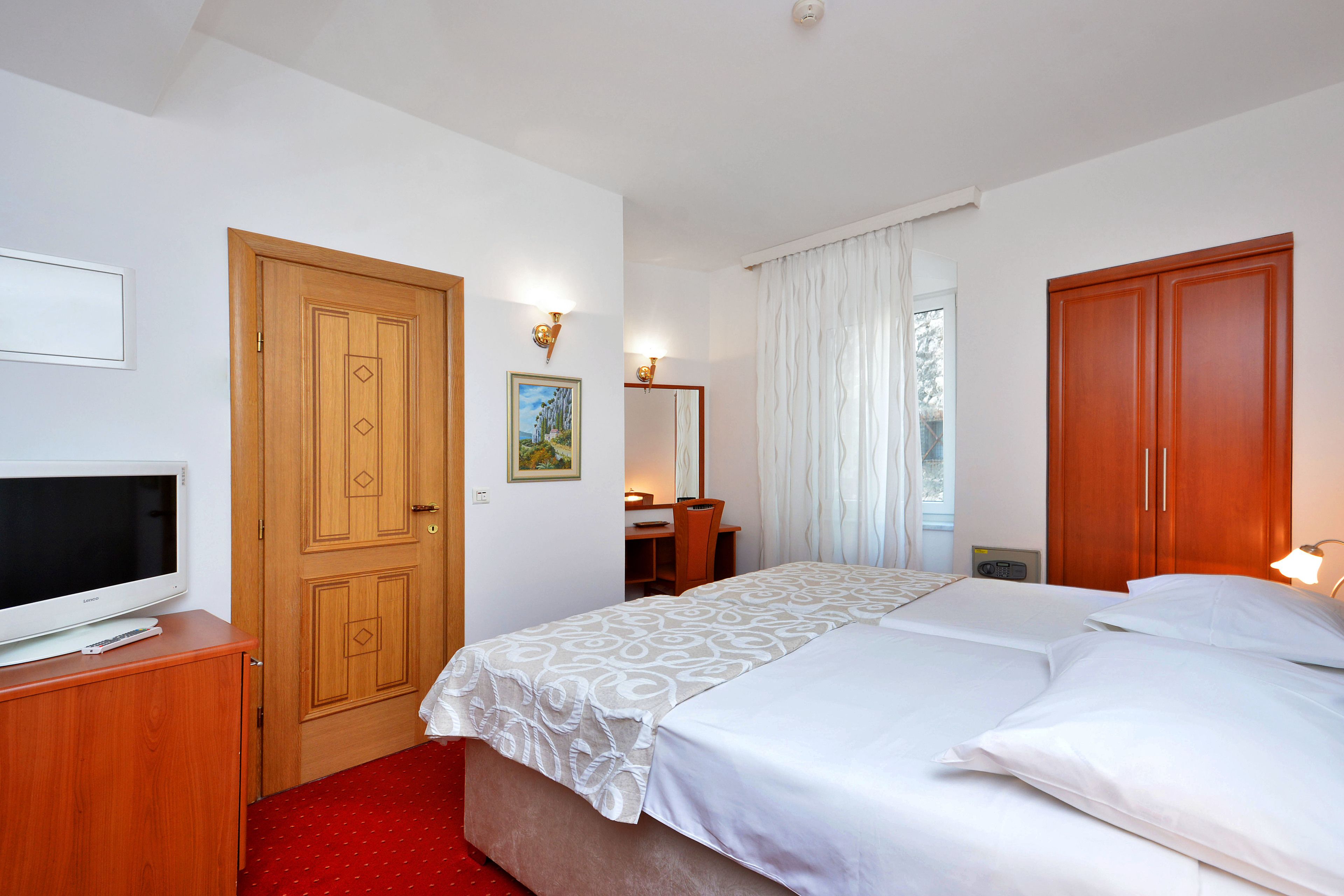 Habitación de hotel con una cama grande, un escritorio con silla, un televisor en un mueble y un armario.