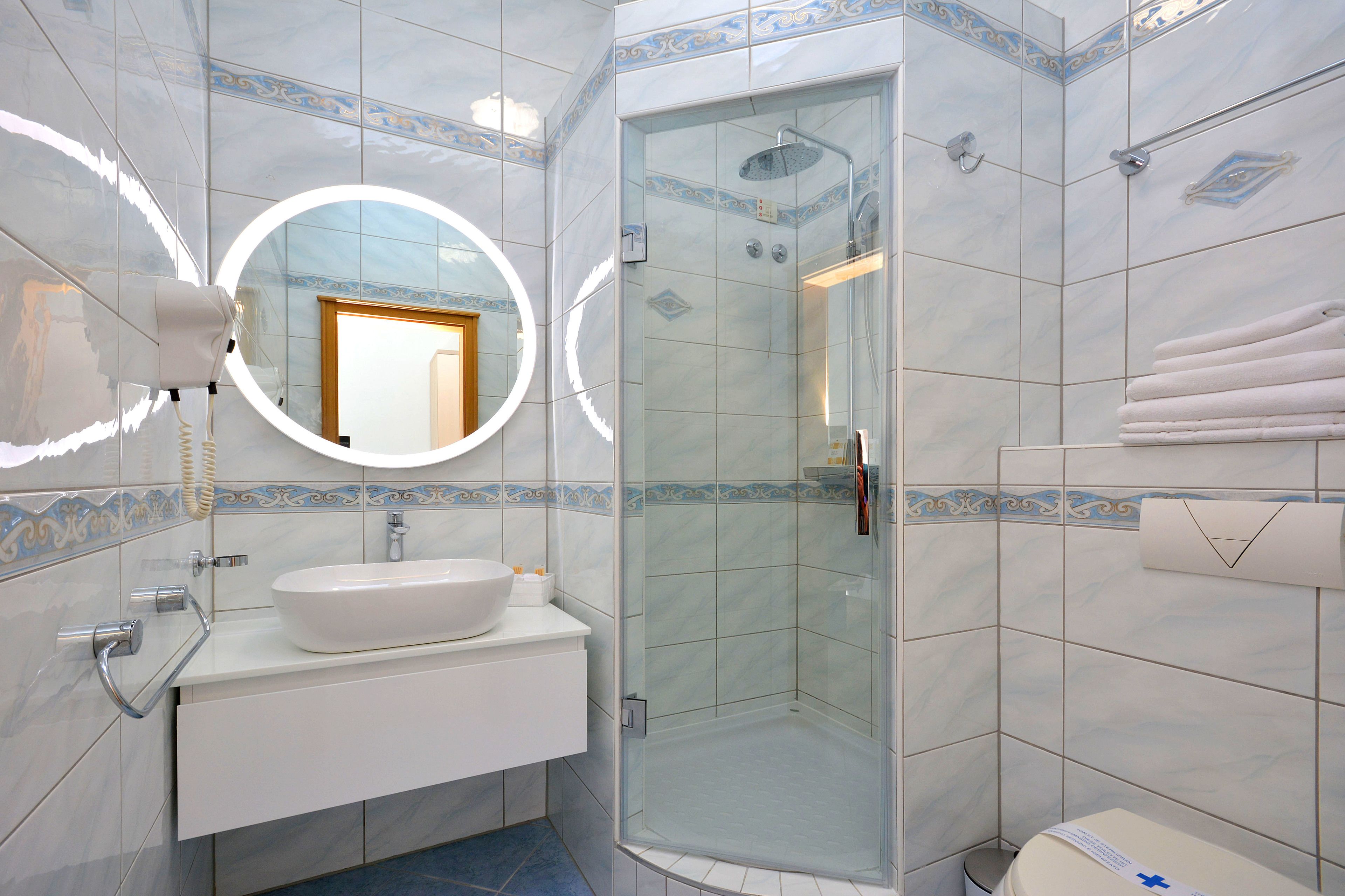 Une salle de bain moderne avec une douche à parois de verre, un miroir rond et un lavabo blanc.
