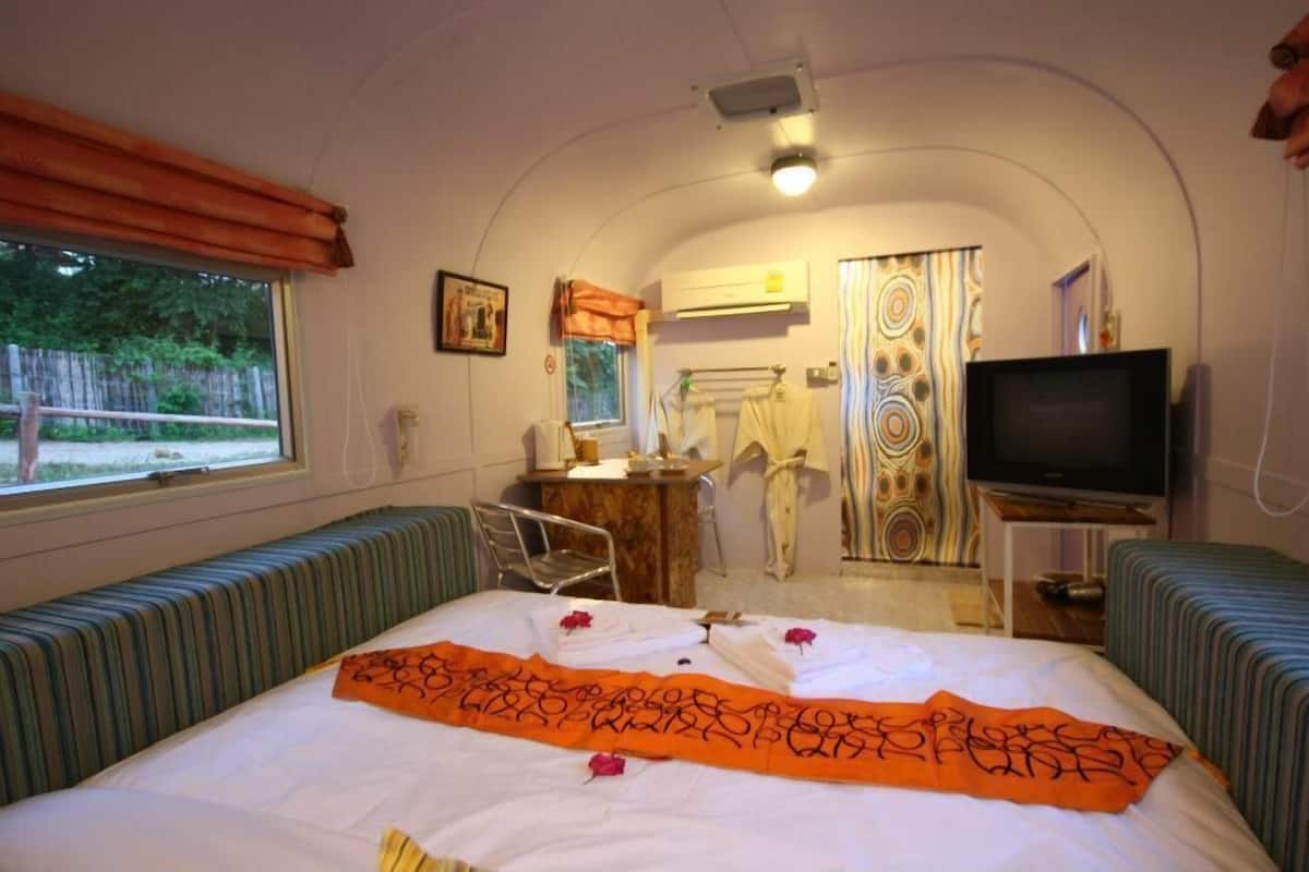 A compact room with a bed, a desk, a television, and a window.