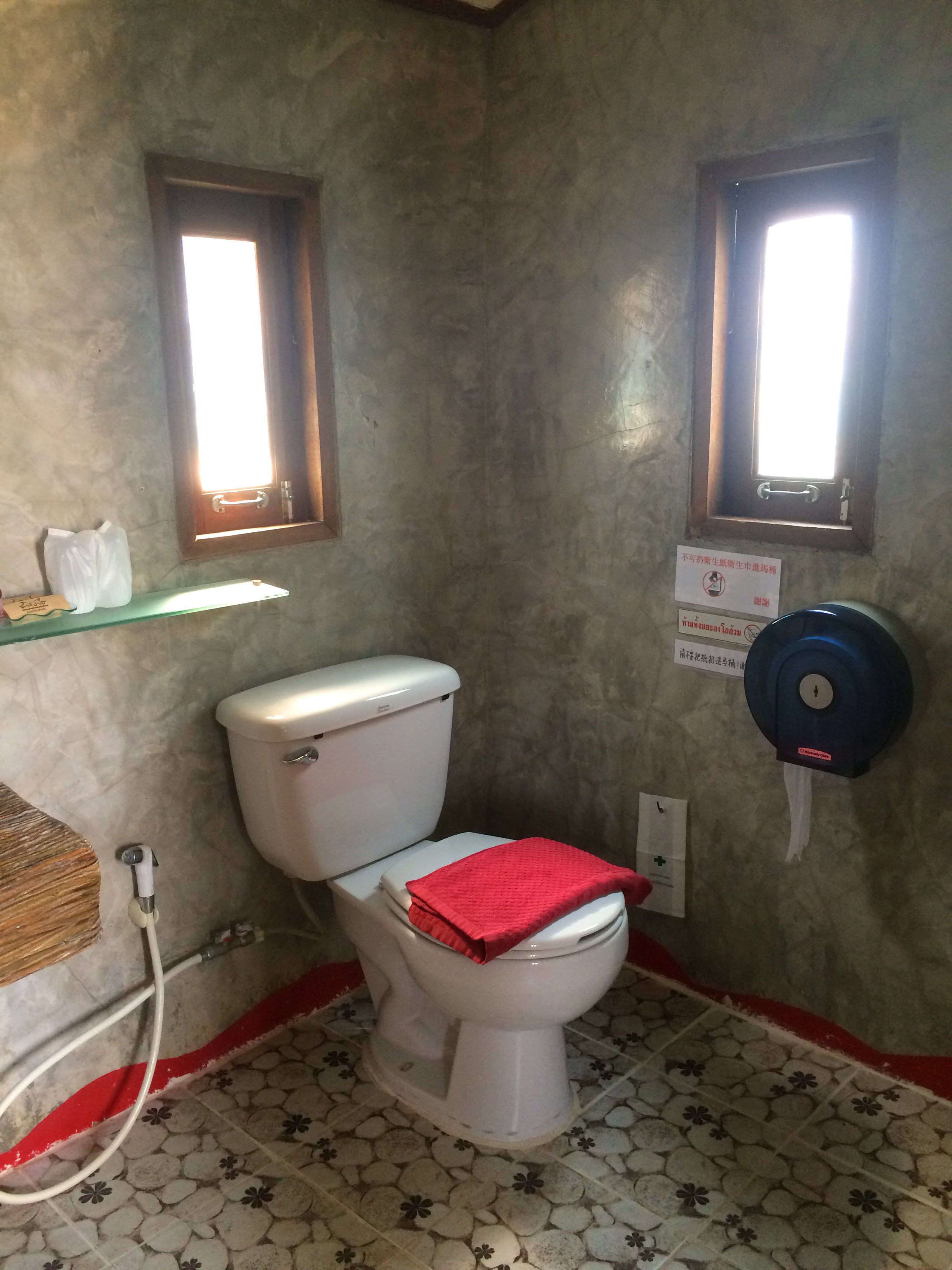 Un baño con un inodoro blanco, una toalla roja sobre el asiento, un secador de manos y un cubo de basura.
