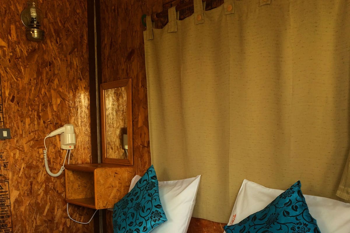 A hotel room with two beds, each with white linens and blue patterned pillows. There is a wooden headboard, a wall-mounted phone, and a curtain.