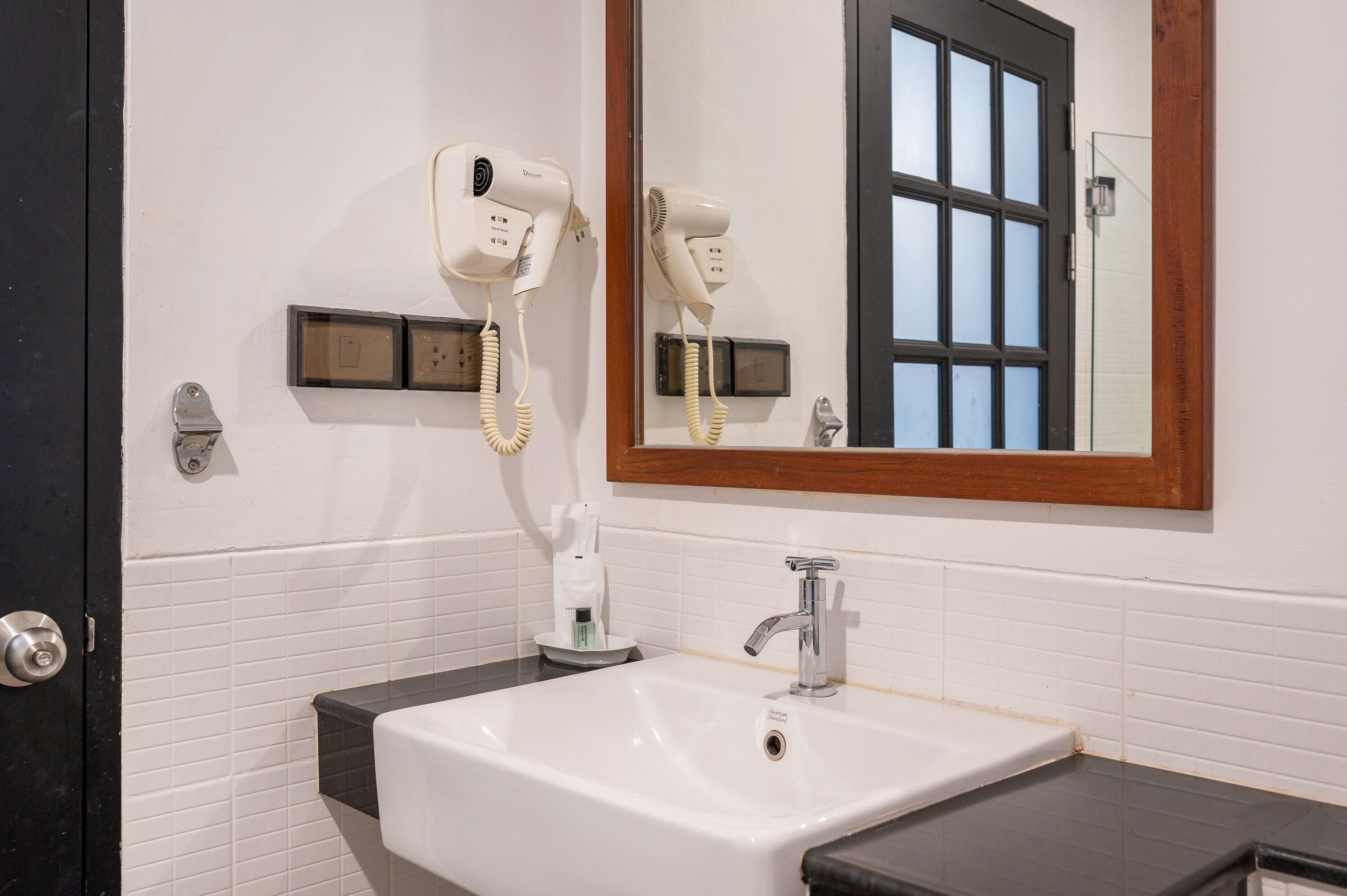 A bathroom with a white sink, a mirror with a wooden frame, and two hair dryers mounted on the wall.