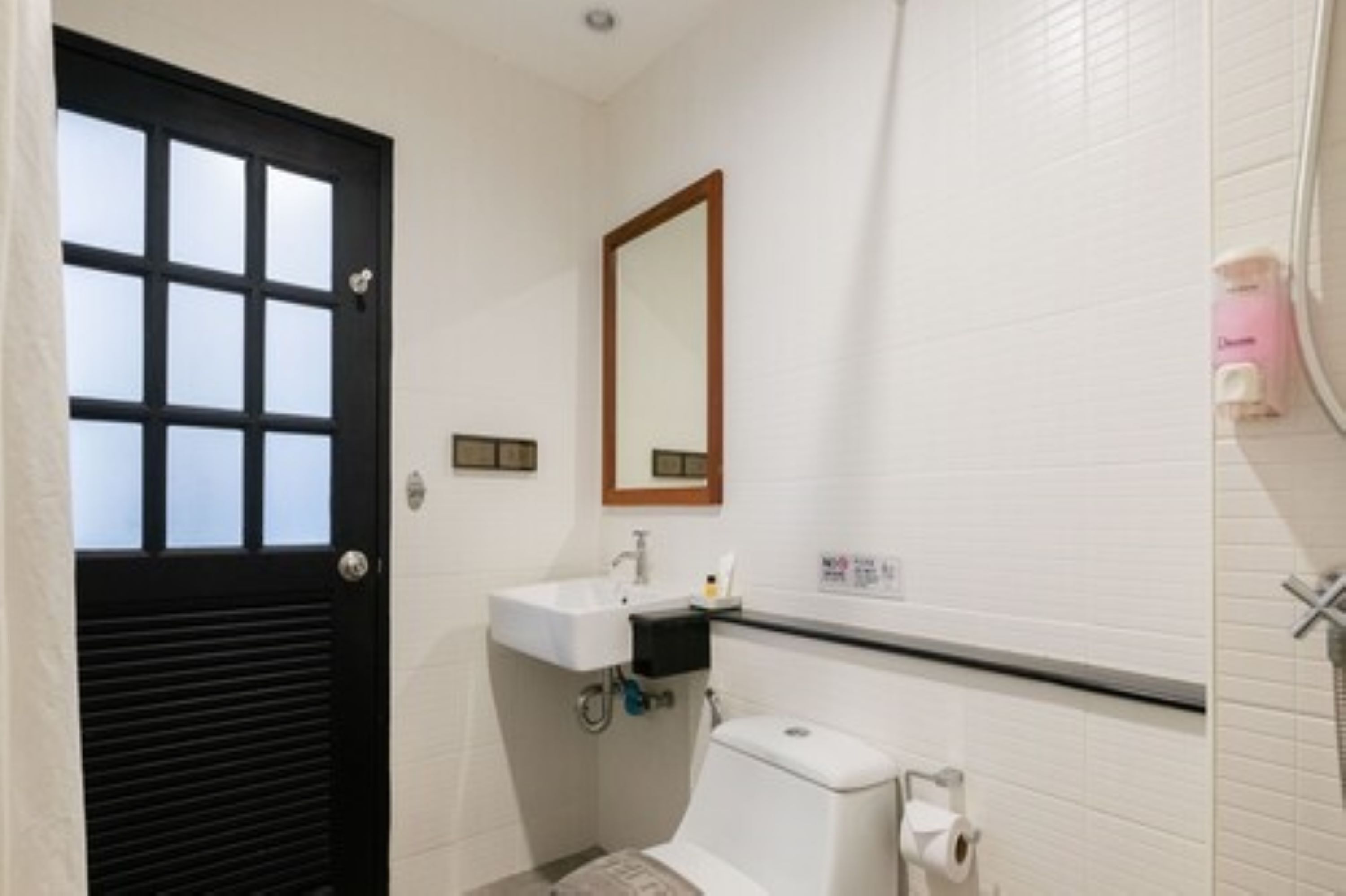 A small bathroom with a white sink, a mirror, a toilet, and a black door with a window.