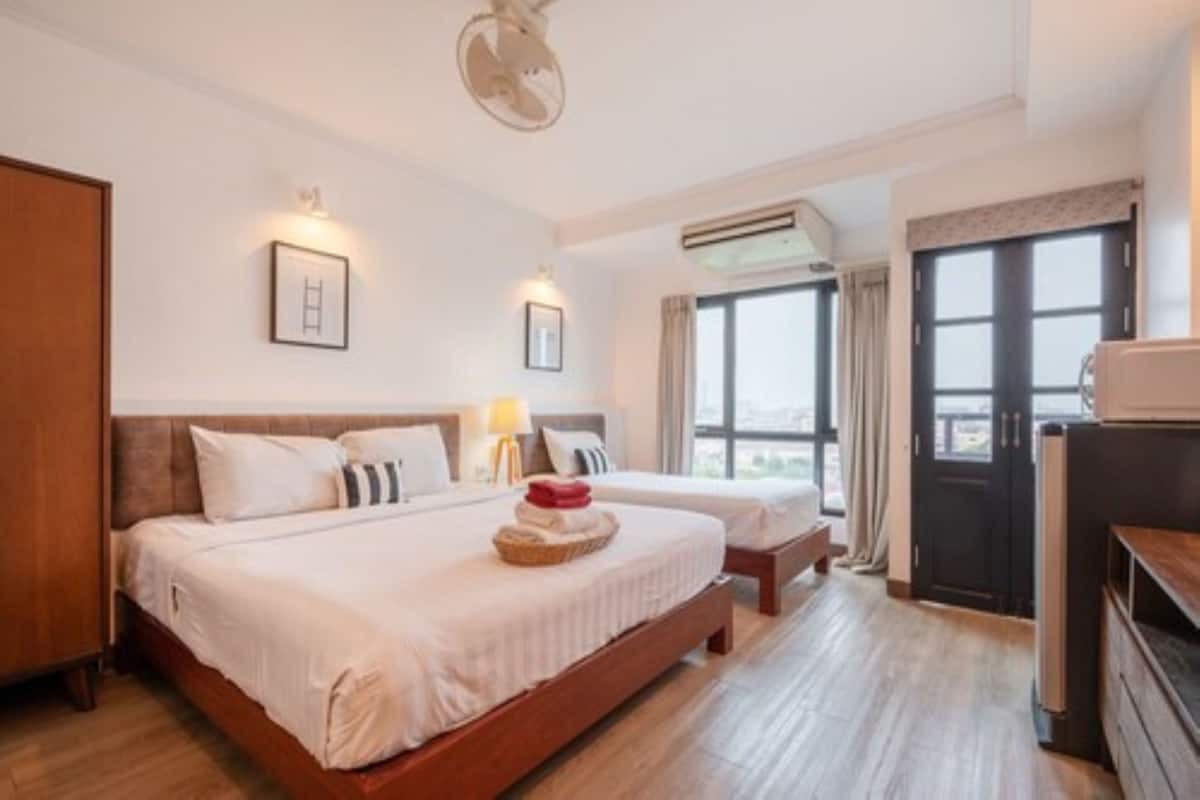 A hotel room with two beds, a wooden floor, a desk, and a window with curtains.