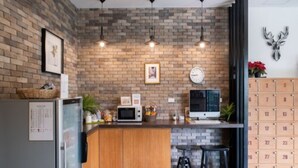 A kitchen with a brick wall, a refrigerator, a microwave, a clock, and a calendar on the wall. - The Corner Lodge (Pattaya)