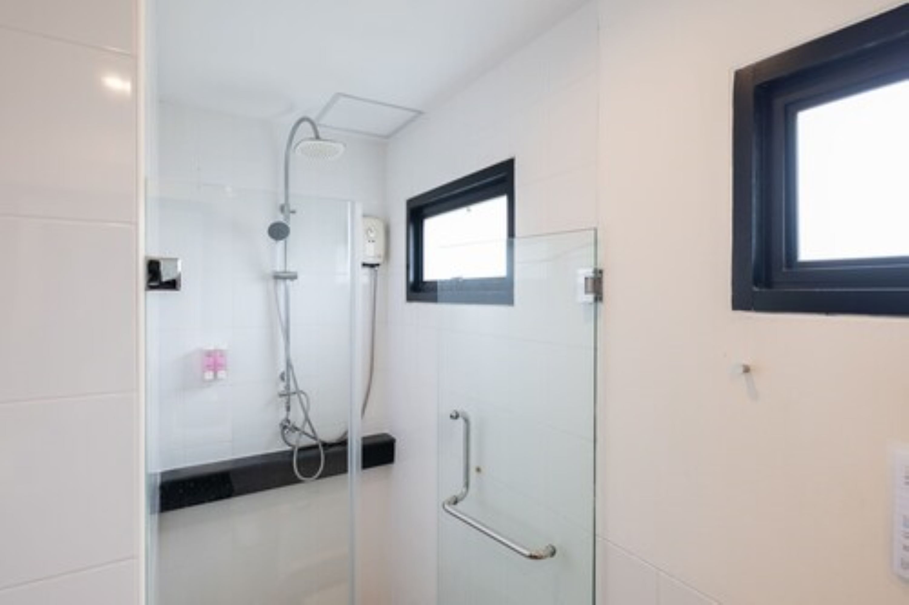 Ein modernes Badezimmer mit Duschkabine aus Glas, Handlauf und Fenster.