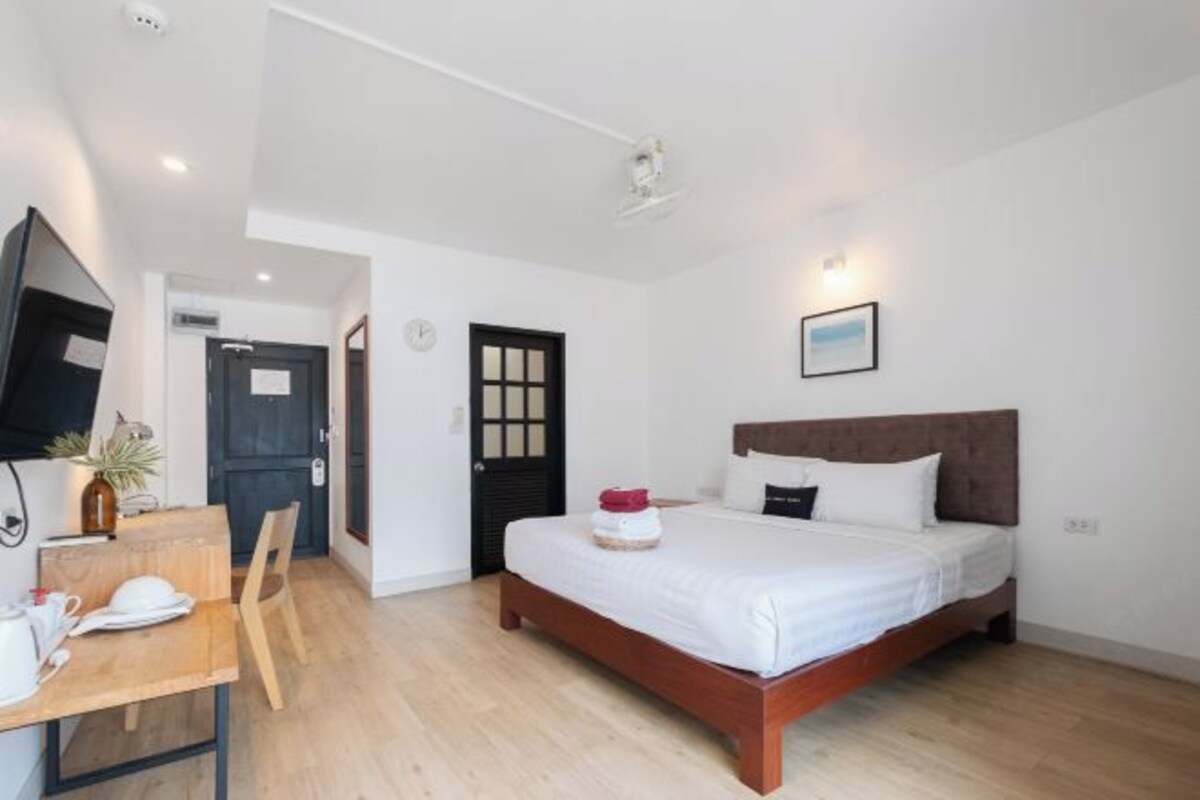 A bedroom with a bed, a desk with a chair, a television, and a door.