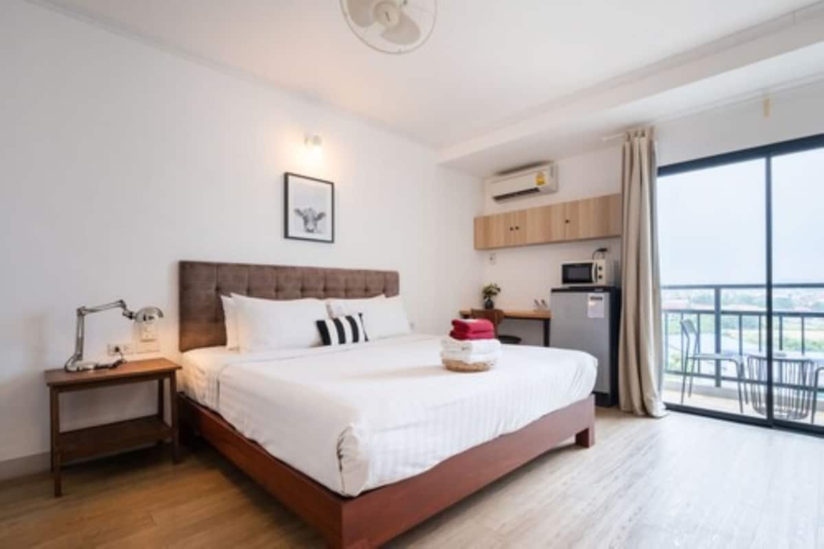 A hotel room with a bed, bedside table, lamp, and a view of the city through large windows.