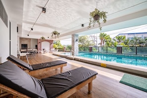 A poolside area with lounge chairs, a brick wall, and a view of a building and trees. - The Corner Lodge (Pattaya)