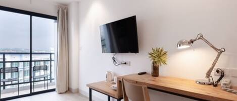 Une chambre d’hôtel moderne dotée d’un grand balcon, d’un téléviseur à écran plat fixé au mur, d’un bureau en bois avec une lampe et d’une plante en pot.