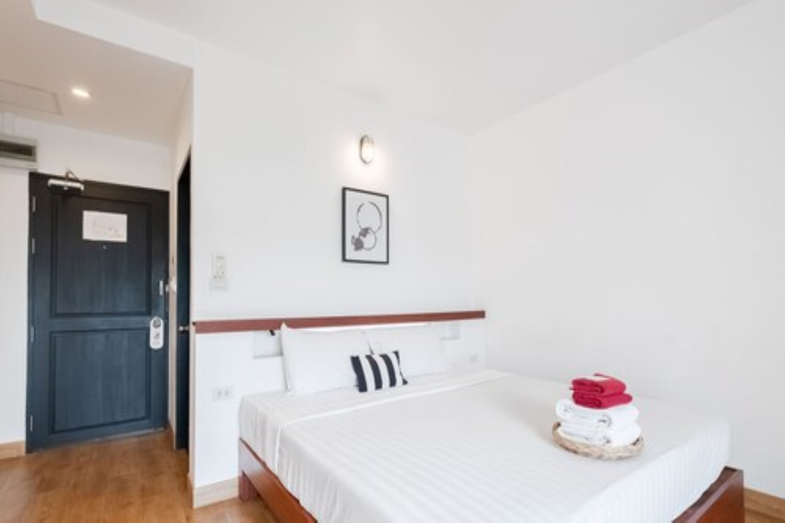 A hotel room with a bed, a door, a wall-mounted light, and a framed picture.