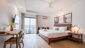 A hotel room with a bed, bedside table, desk, chair, and a potted plant. - The Corner Lodge (Pattaya)