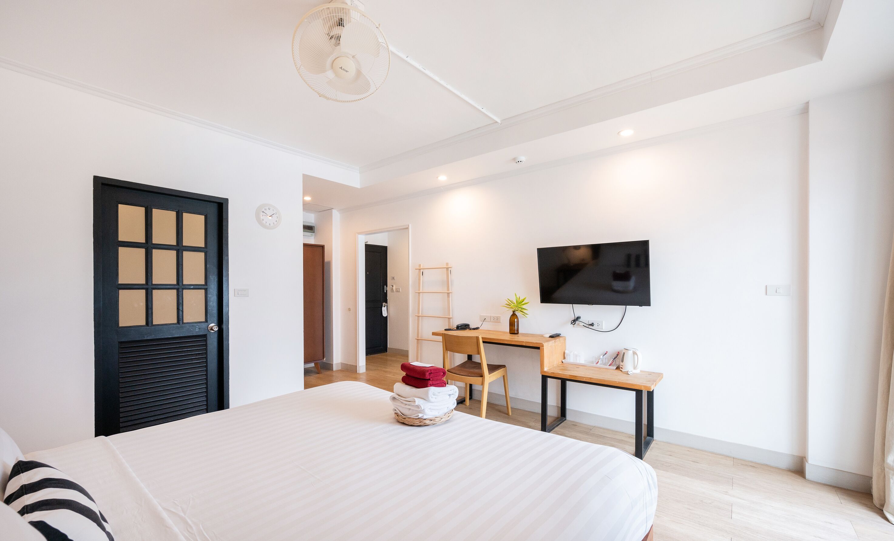 A modern bedroom with a large bed, a desk with a computer, a TV, and a small plant.