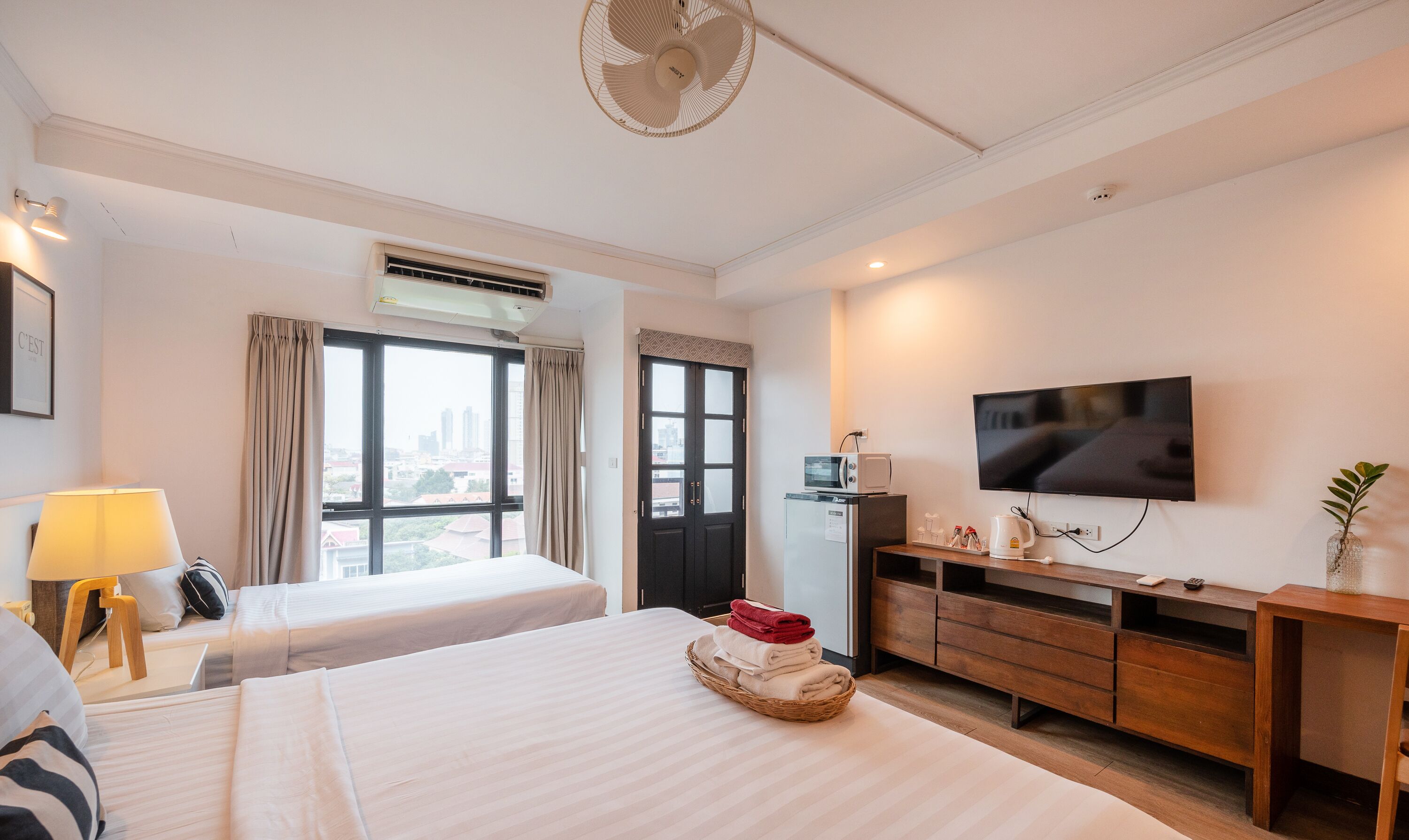 A hotel room with two beds, a TV, a desk with a microwave, and a view of the city.