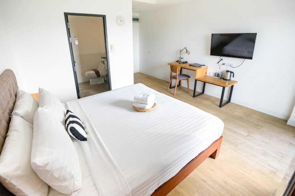 A hotel room with a bed, a desk, a chair, a television, and a bathroom visible through an open door.