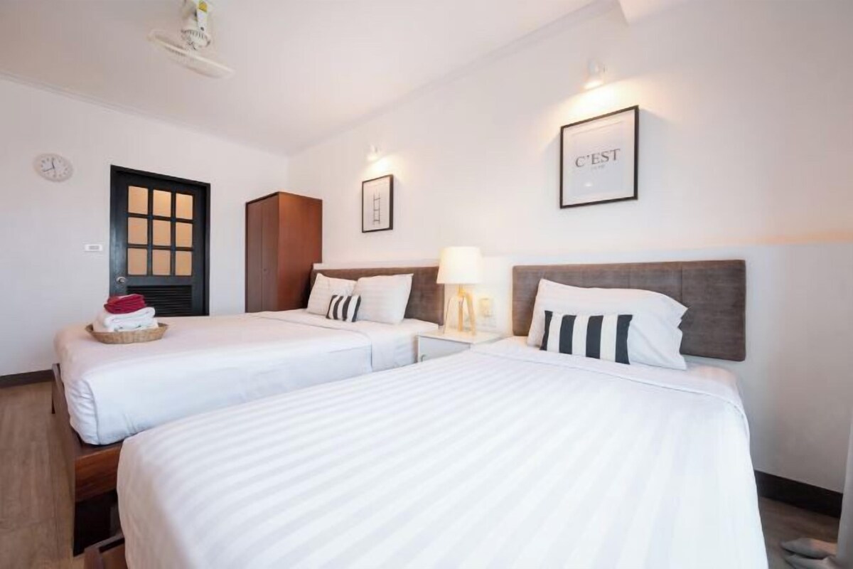 A hotel room with two beds, a wooden door, a framed picture, and a wall clock.
