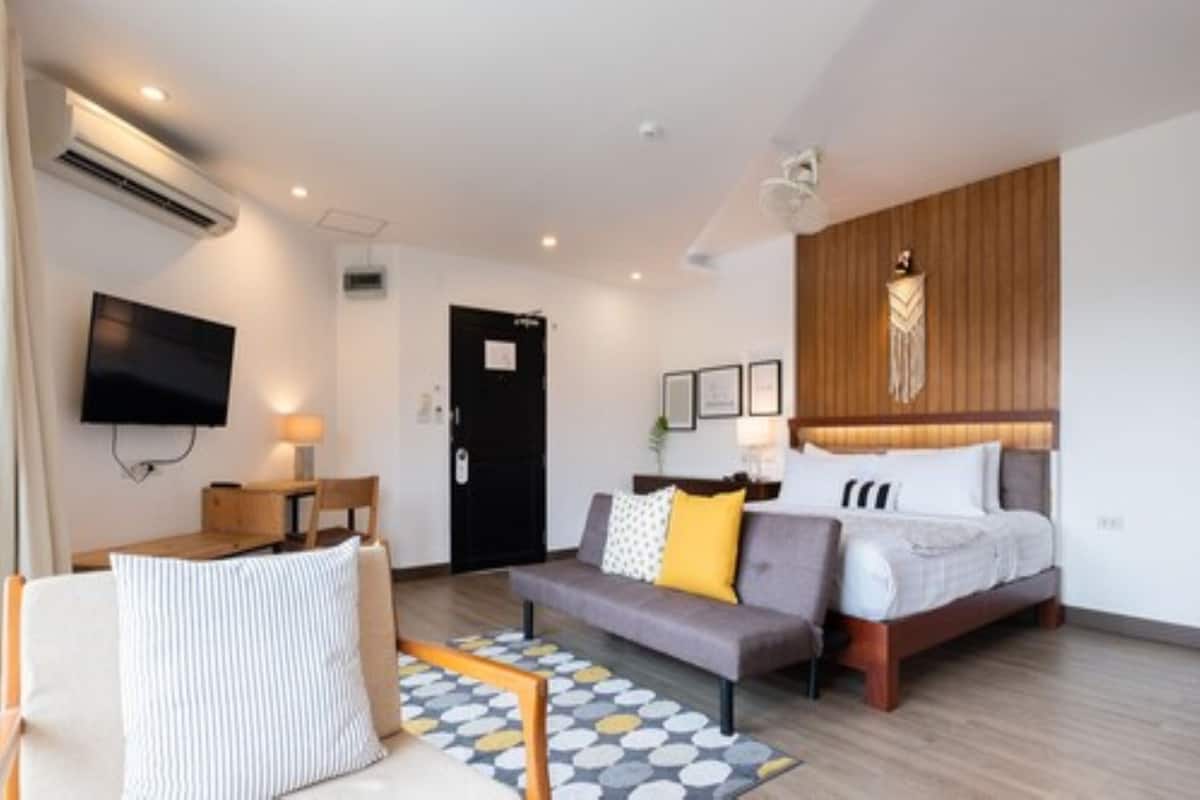A modern hotel room with a bed, a sofa, a TV, and a desk.