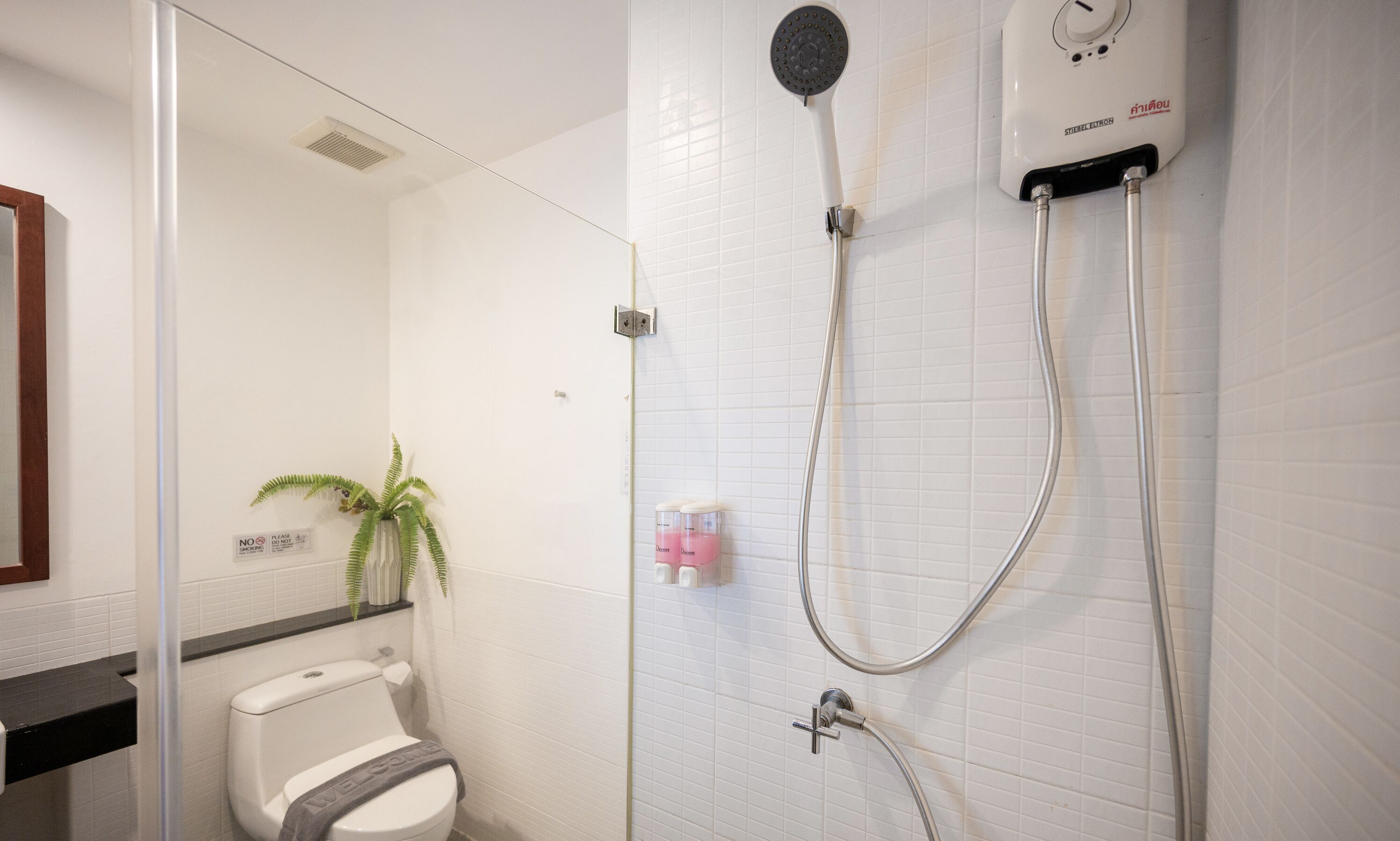Un baño con inodoro, ducha con cabezal de ducha de mano y lavamanos con espejo.