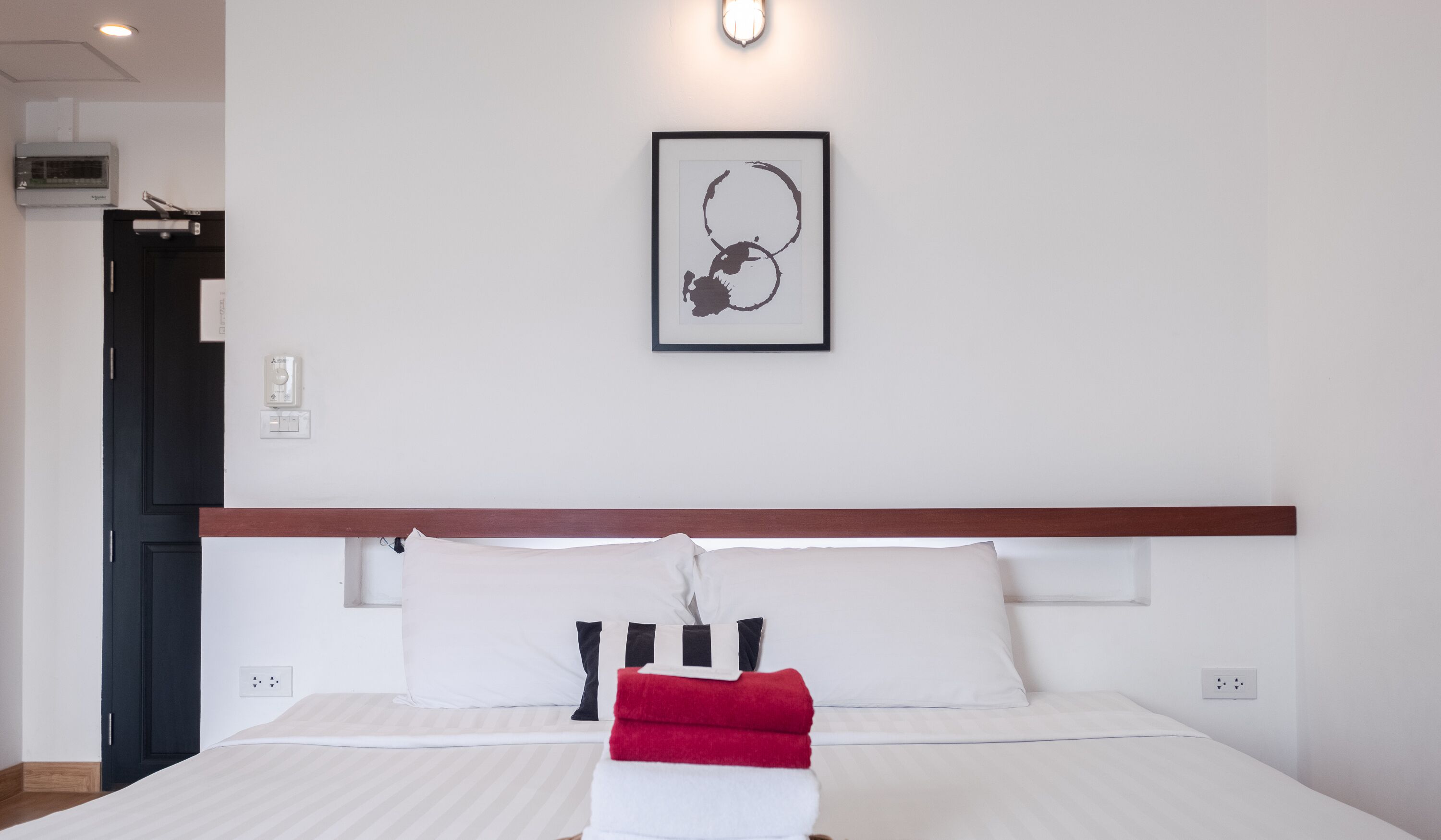 A hotel room with a bed, a framed artwork on the wall, and a door to the left.