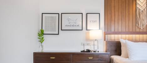 A neatly arranged hotel room with a wooden headboard, a bedside table with a lamp, and three framed pictures on the wall.