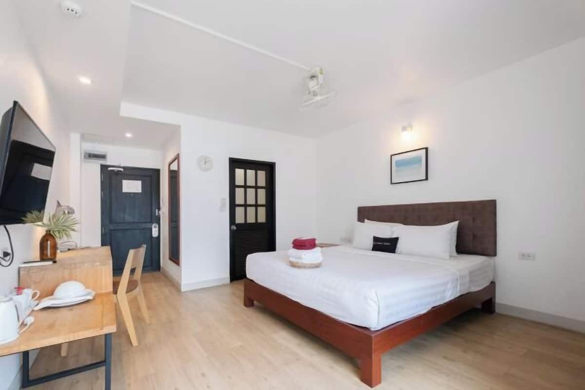 A bedroom with a bed, a desk with a chair, a television, and a door.