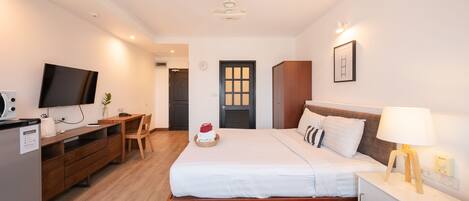 A hotel room with two beds, a desk, a television, and a small kitchenette.