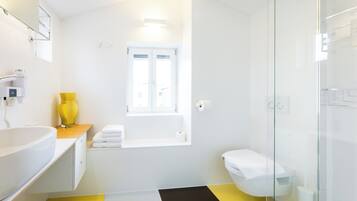 Une salle de bain moderne avec un lavabo blanc, un vase jaune, des toilettes blanches et une cabine de douche en verre.