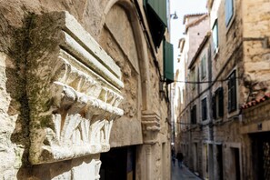 A narrow street with historic stone buildings, a visible archway, and a person walking in the distance.