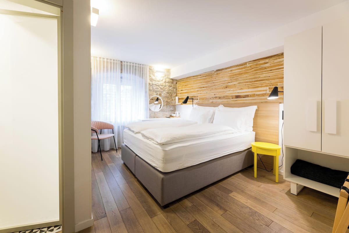 A modern bedroom with a bed, bedside table, lamp, and a small seating area.