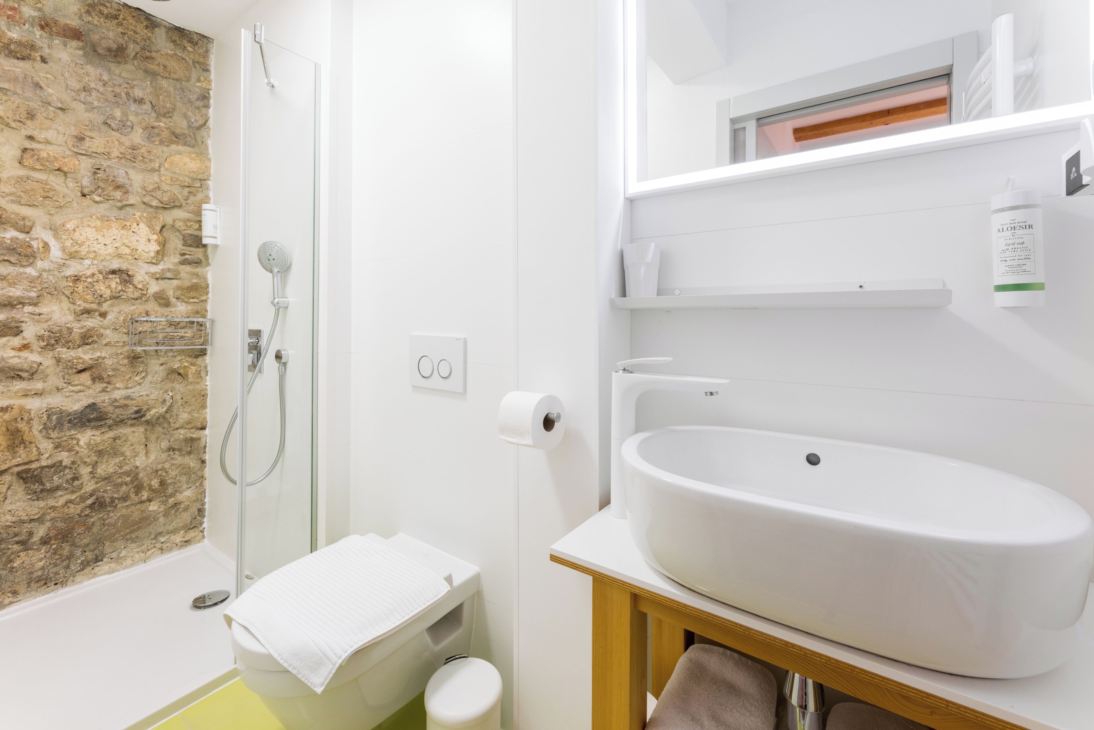 A bathroom with a stone wall, a shower, a toilet, and a sink.