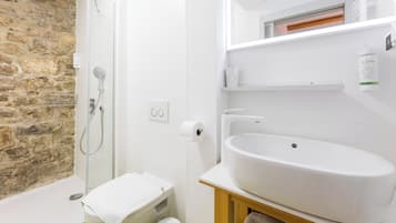 A bathroom with a stone wall, a shower, a toilet, and a sink.