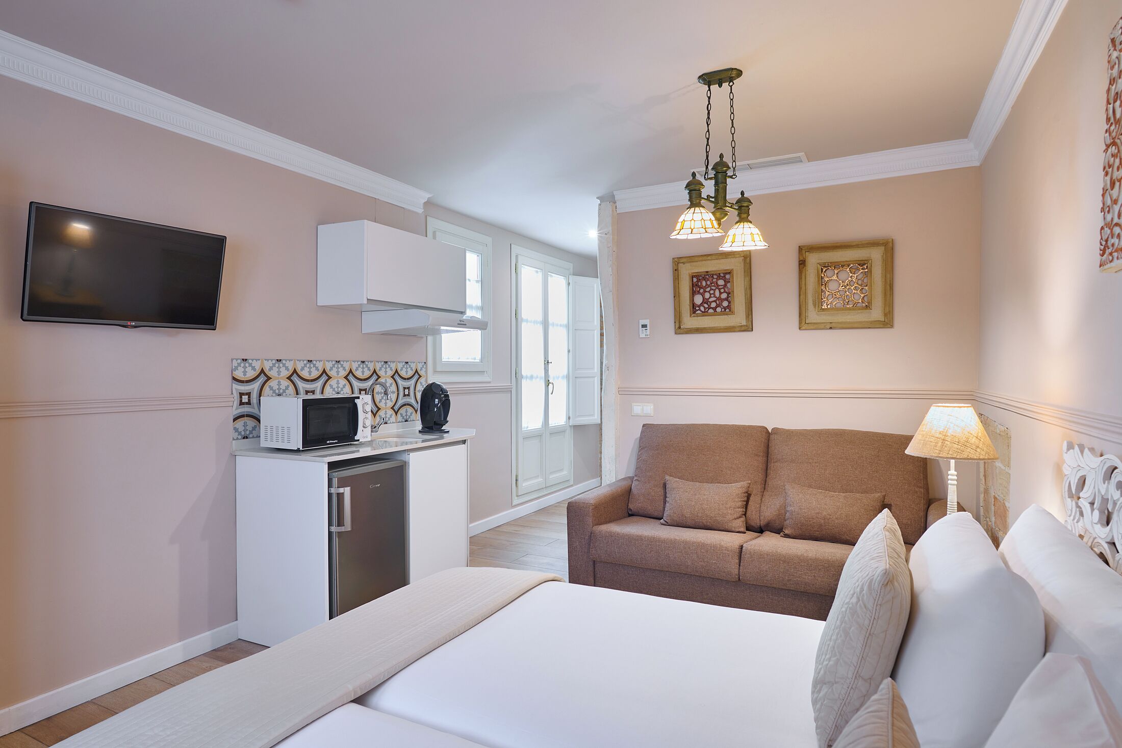 Un dormitorio con cama, sofá, televisión, microondas y lámpara.