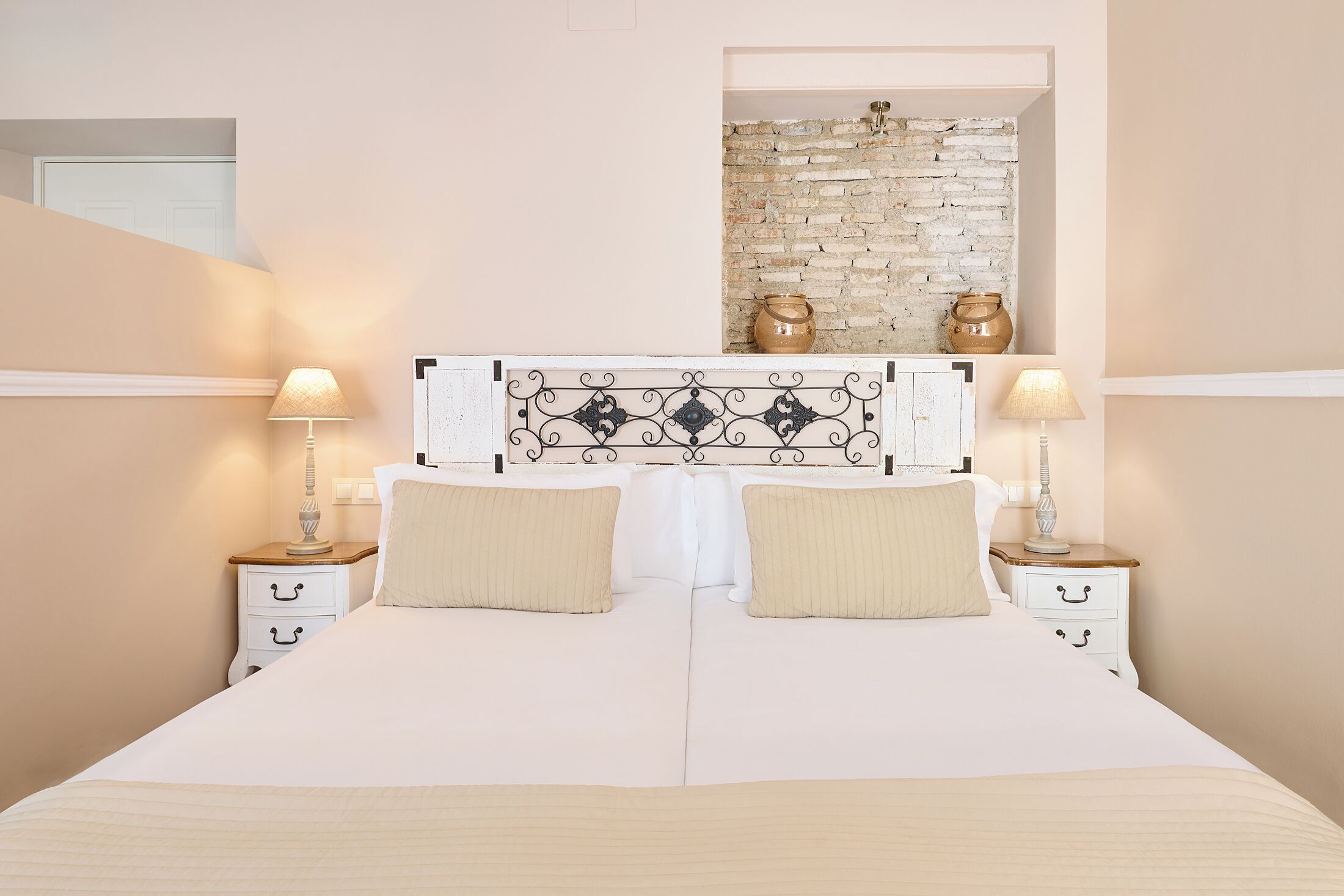 A bed with a white headboard, two bedside tables with lamps, and a brick wall above the bed.